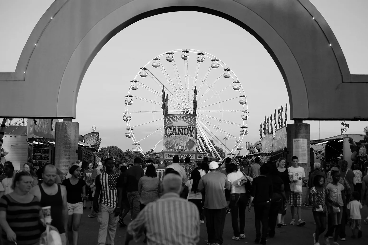 Fairgoers walk through the entrance arch toward the Ferris wheel and midway at the fair on the Winston-Salem Fairgrounds.