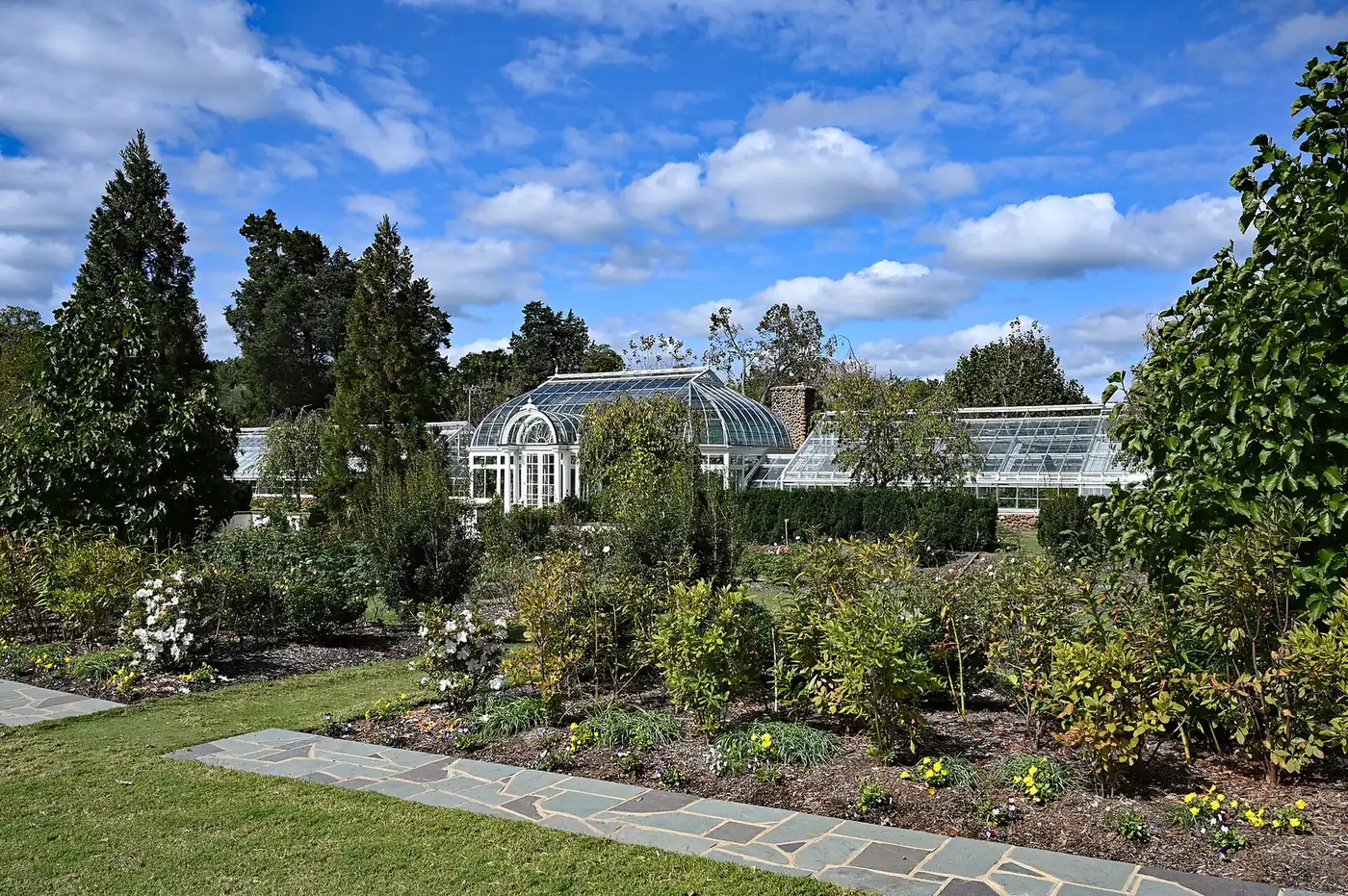 Flower beds and stone paths in the formal gardens at Reynolda, with the glass conservatory behind, in Winston-Salem.
